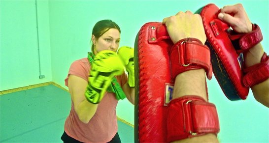 Eine Person mit gelben Boxhandschuhen steht vor Händen, die rote Pratzen tragen.